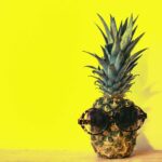 green pineapple fruit with brown framed sunglasses beside yellow surface