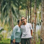 selective focus photo of old couple standing together with trees in the background